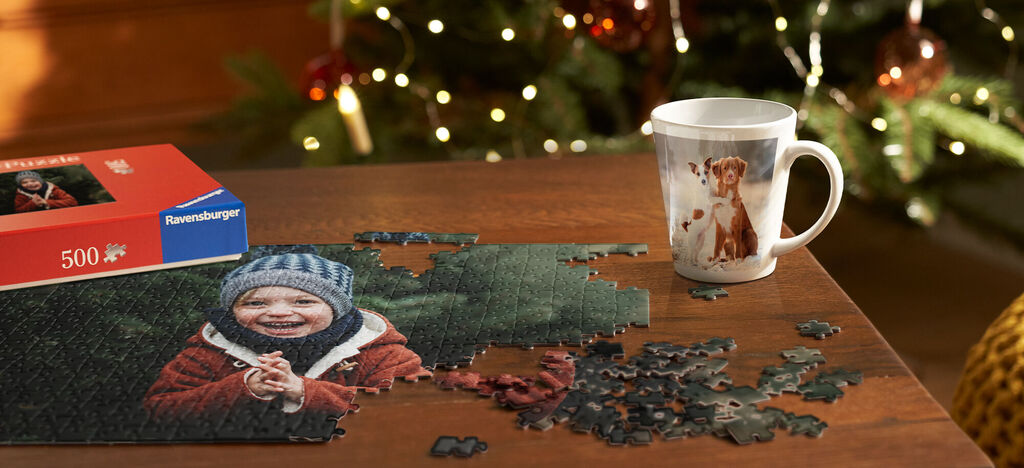 Šťastný chlapec s čiapkou sedí pri stole, pozerá na puzzle so zvieratkom a vedľa má šálku s motívom psa.