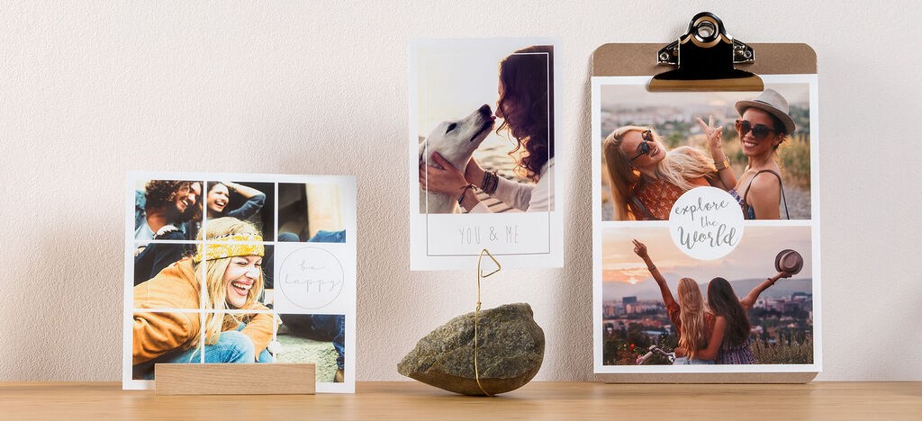 Tri personalizované fotoprodukty na stole. Vľavo fotokoláž, v strede fotka ženy so psom, vpravo plagát s textom 'explore the world'.