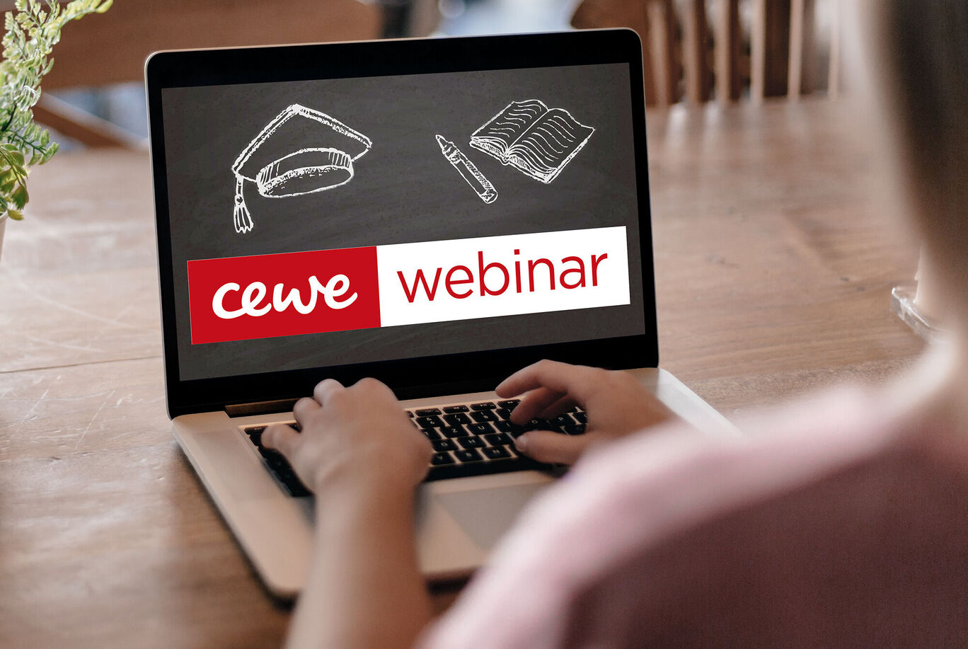 Osoba pri notebooku sa zúčastňuje na CEWE webinári, stôl s poznámkami a kresliacimi potrebami.