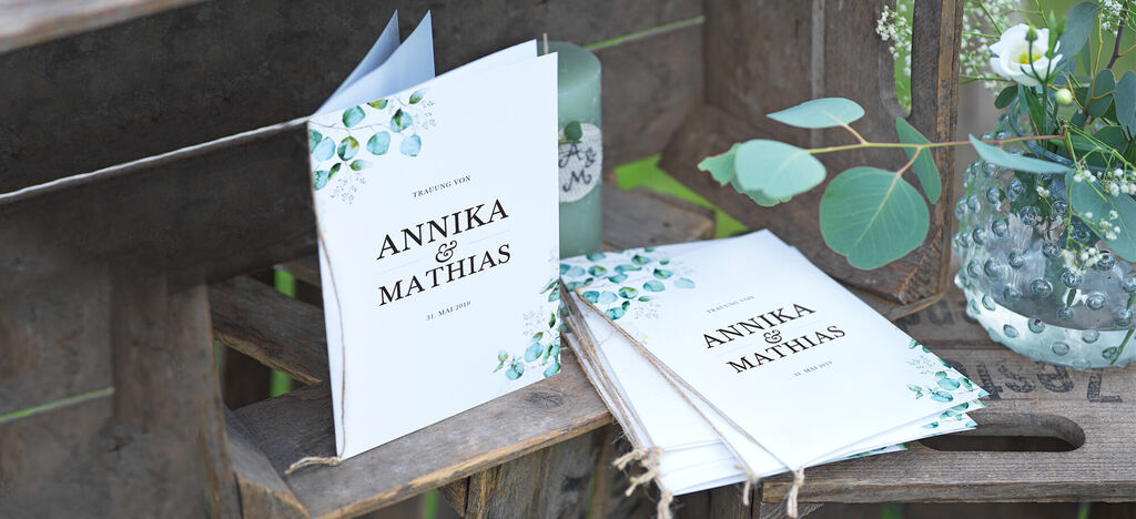 Dve personalizované CEWE pohľadnice s textom "ANNIKA & MATHIAS" na drevenej lavici obklopenej rastlinami.