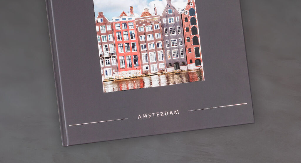 Fotokniha CEWE s fotkou farebných domov Amsterdamu na elegantnom šedom pozadí.