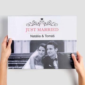 Osoba drží CEWE Fotoknihu s názvom "Just Married". Vnútri sú romantické farby a elegantný dizajn.