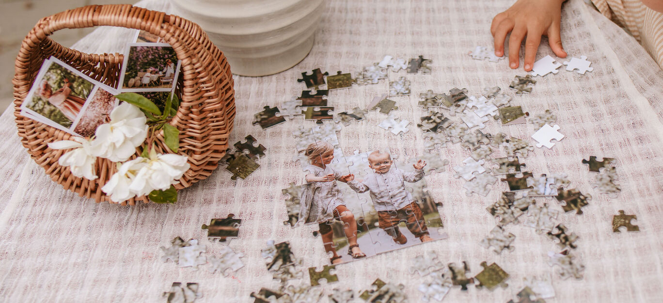 Dieťa skladá puzzle z fotografií na stole. Vidno aj kvety a kôš.