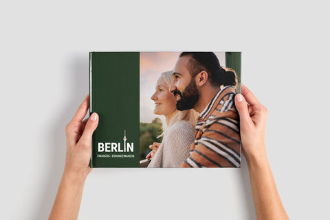 Osoba drží CEWE fotoknihu s obálkou v zelenej farbe a nápisom 'Berlín'.