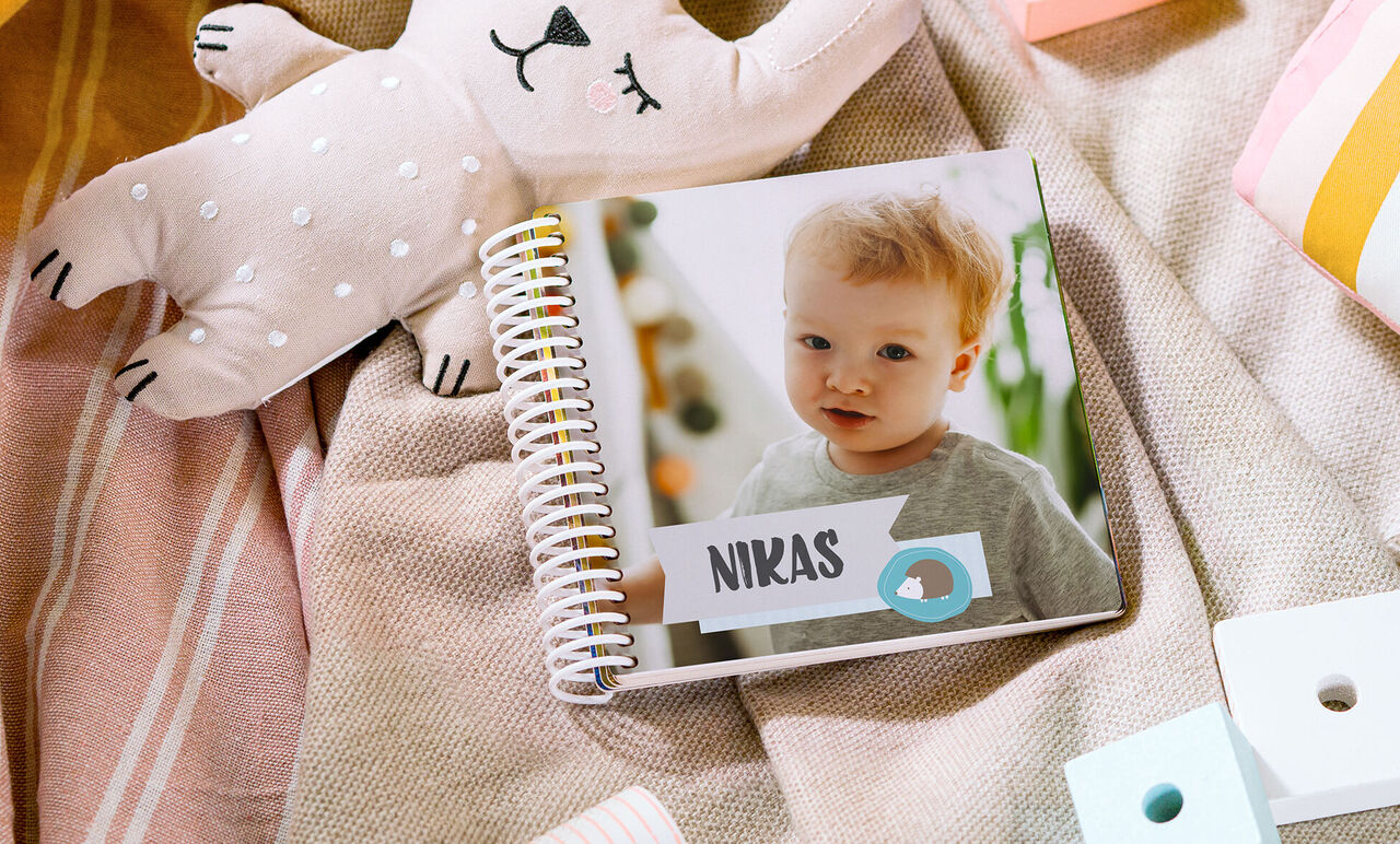 S láskou navrhnutá fotokniha s menom Nikas na obale, obklopená textíliami a plyšákom.
