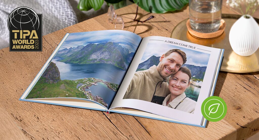 Otvorená fotokniha zobrazuje horskú krajinu, jazero a pár objímajúci sa. V rohu je ocenenie za najlepšie fotoknihy.