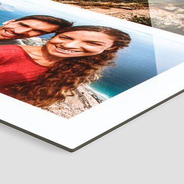 Šťastný pár sa usmieva do kamery, oceán sa trblieta v pozadí. CEWE fotokniha.