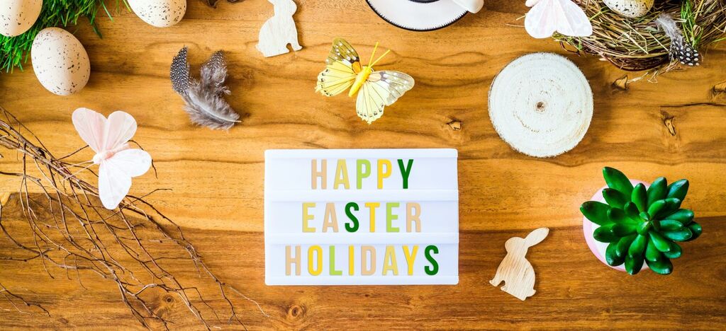 Veľkonočná stolová dekorácia s nápisom "Happy Easter Holidays", farebnými prvkami a roztomilými figúrkami.