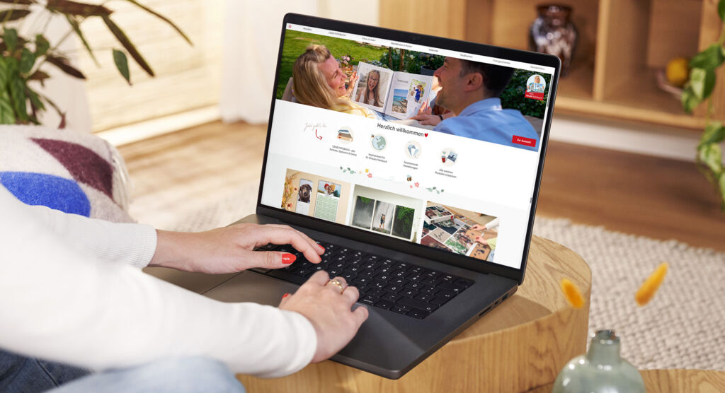 Osoba sedí pri stole a pozerá si web CEWE na notebooku pre tvorbu kreatívnych produktov.