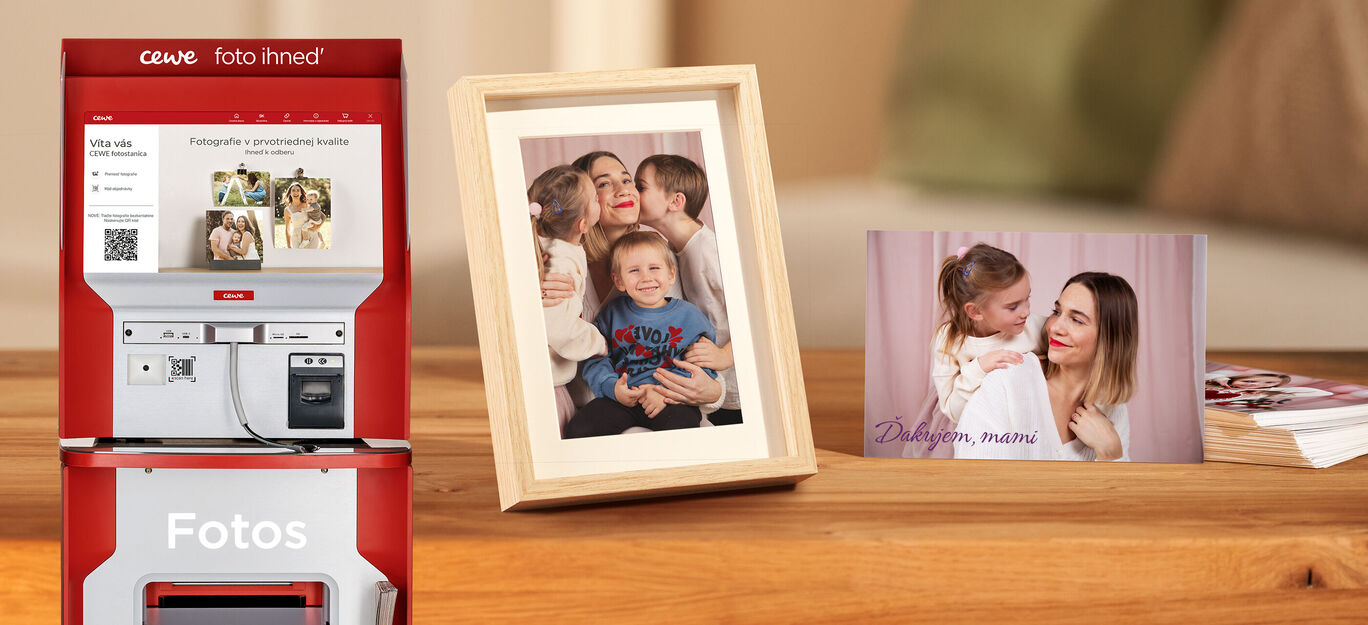CEWE fotokniha s rodinnými fotografiami, zarámovaný obrázok na stole a viacero pohľadníc.