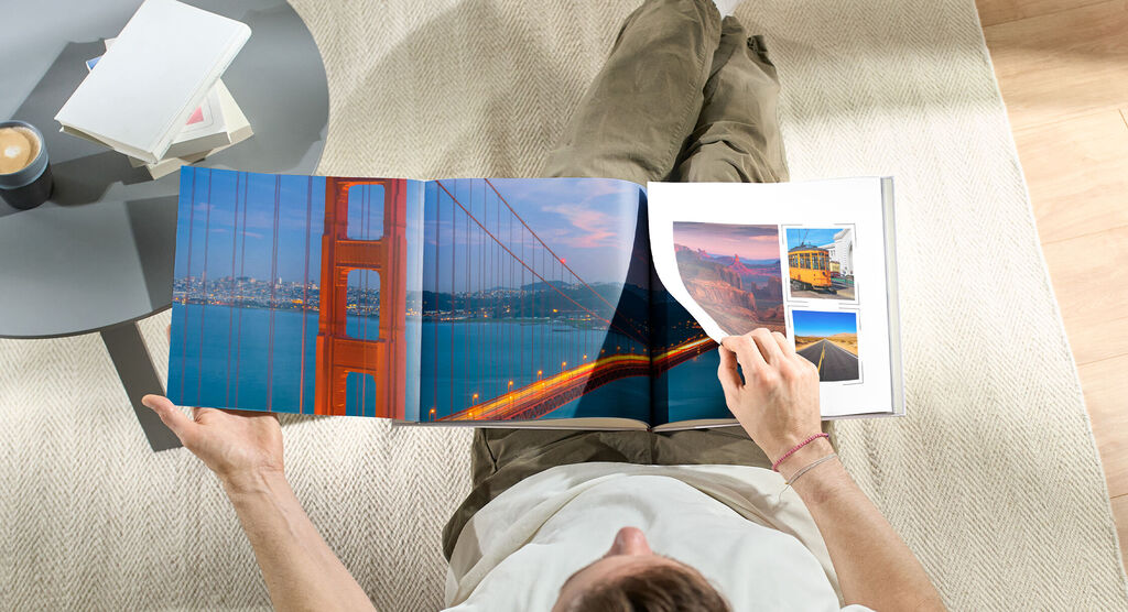 Osoba listuje vo CEWE FOTOKNIHE s fotografiami mosta Golden Gate a ďalšími cestovnými okamihmi.