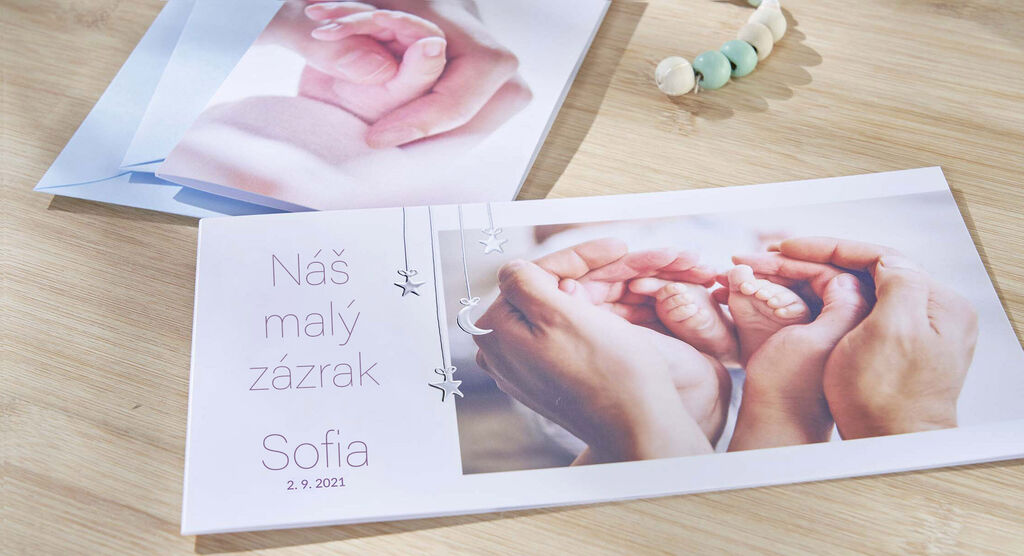 Dve ruky nežne držia ruky bábätka v CEWE fotoknihe.