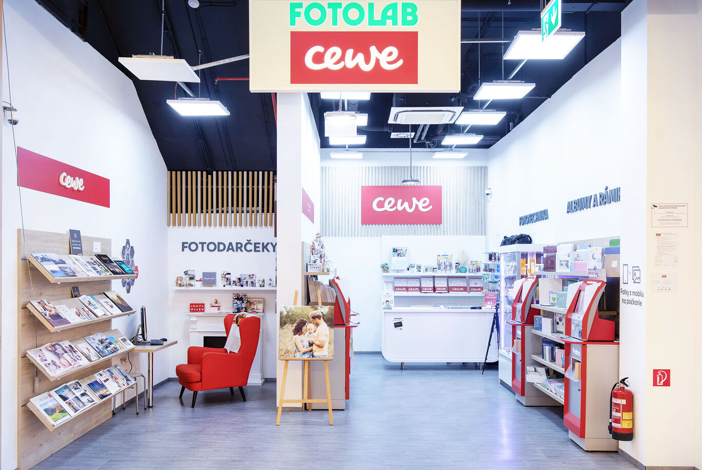 Interiér CEWE Fotolab s regálom a červenou stoličkou