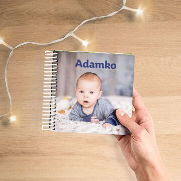 Osoba drží CEWE fotoknihu s menom Adamko.