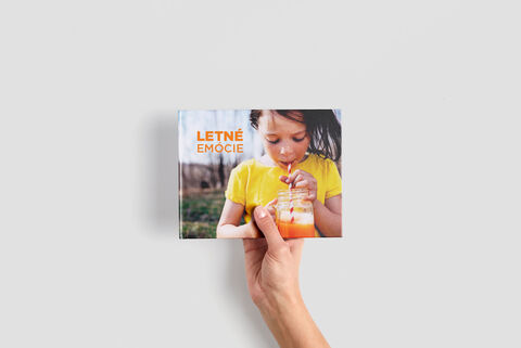 Ruka drží fotoknihu s názvom „Letné Emócie“ a farebným obalom.