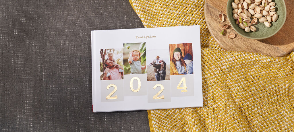 CEWE fotokniha so zlatými číslami 2024 a fotografiami šťastných chvíľ.