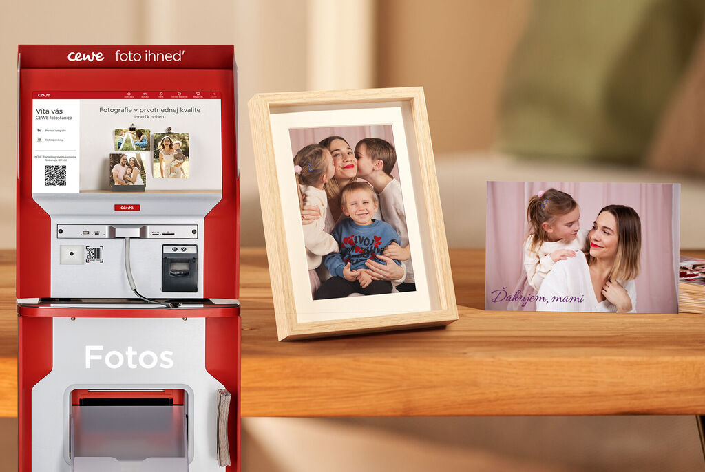 Fotoautomat CEWE s ukážkovými fotkami na stole.