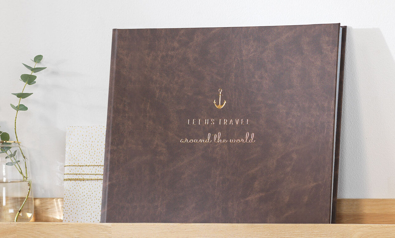 Kvalitná fotokniha s názvom 'Jeremy's Travel around the world' v hnedej koži na poličke.