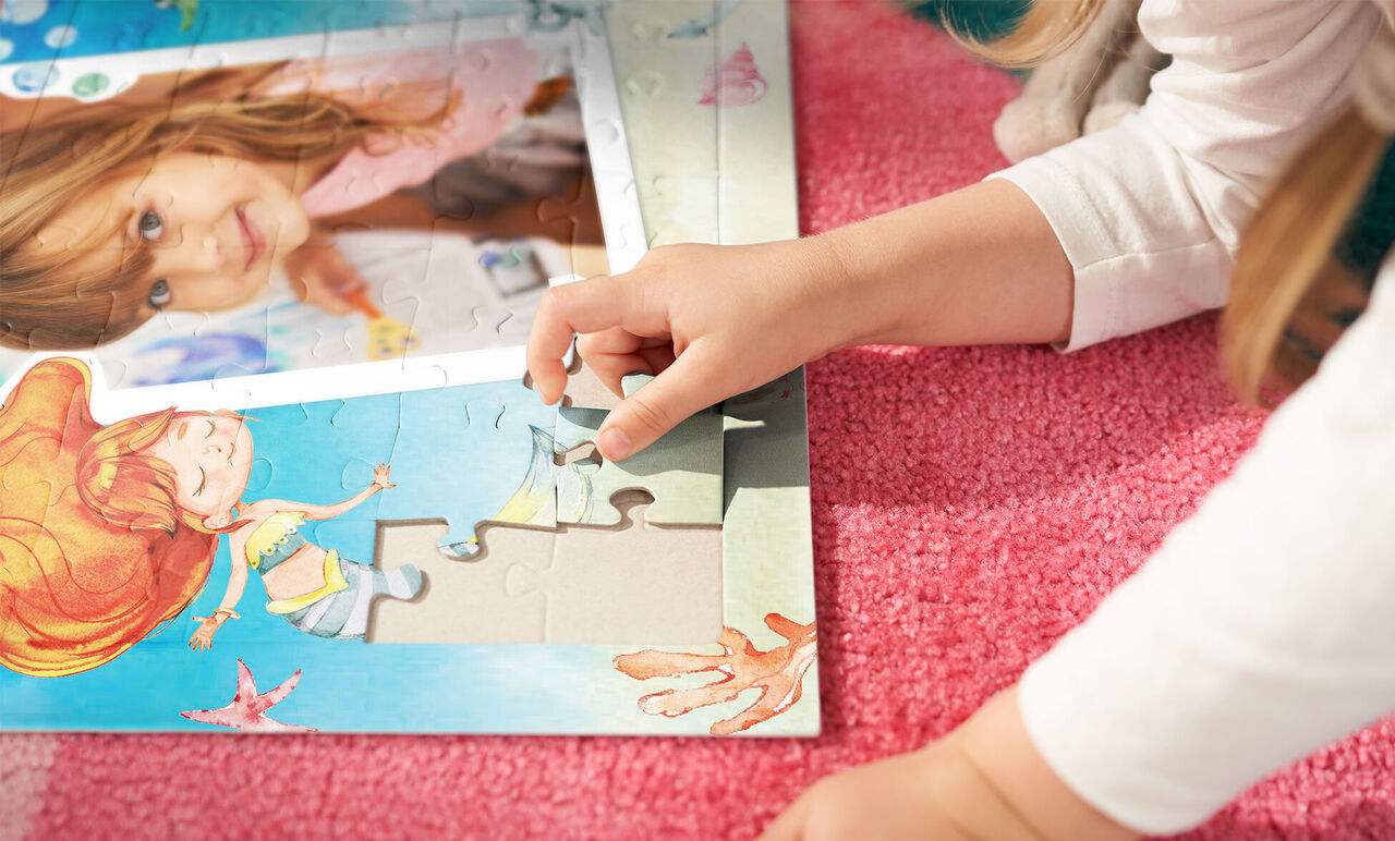 Dieťa leží na ružovom koberci a vkladá kúsoček do pestrého puzzle. Puzzle ukazuje morský svet a dievča.