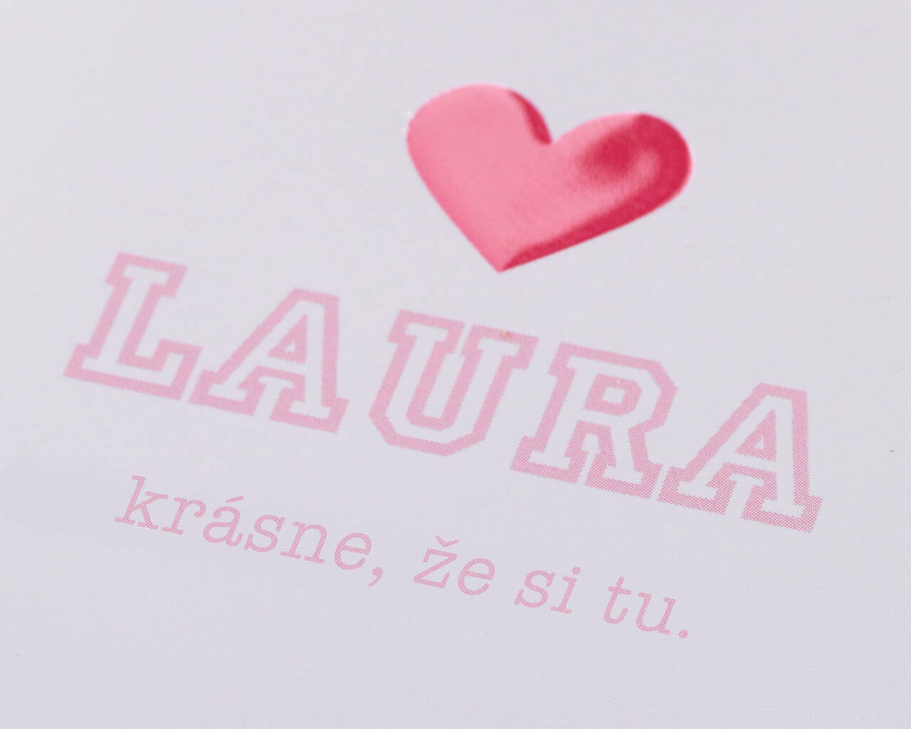 Ružové srdce a meno 'LAURA' na karte. Pod textom je nápis 'krásne, že si tu' v priateľskom písme.