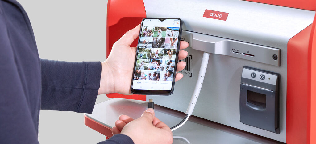 Osoba spája svoj smartphone s CEWE fototlačiarňou na výber fotiek.