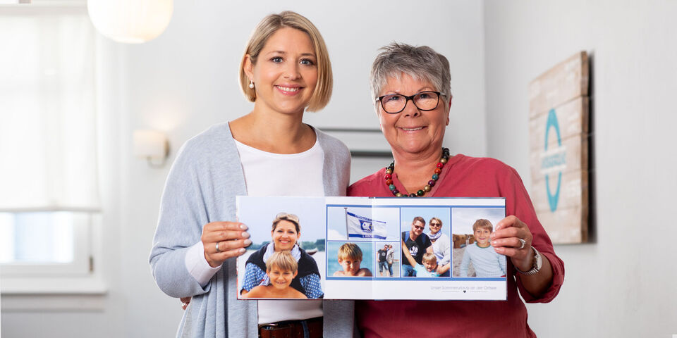 Dve ženy držia otvorenú fotoknihu s rodinnými fotografiami.