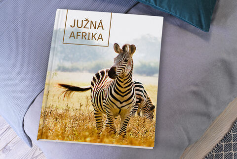 CEWE fotokniha so zebrami na obálke, položená na útulnej pohovke.