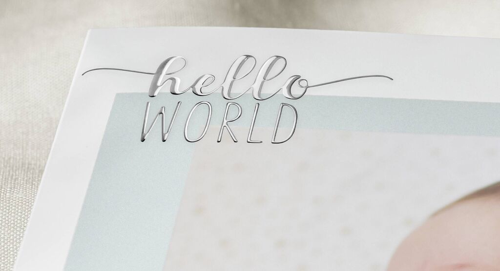 Stránka fotoknihy so štýlovým rukopisom 'hello WORLD', doplnená svetlým rámikom.