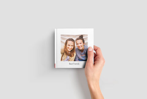 Ruka drží CEWE FOTOKNIHU s fotografiou najlepších priateľov na obálke.