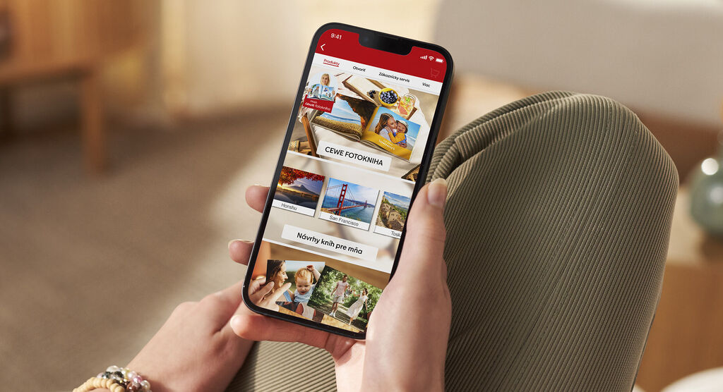 Osoba drží smartfón s aplikáciou CEWE, ktorá zobrazuje rôzne fotoprodukty.