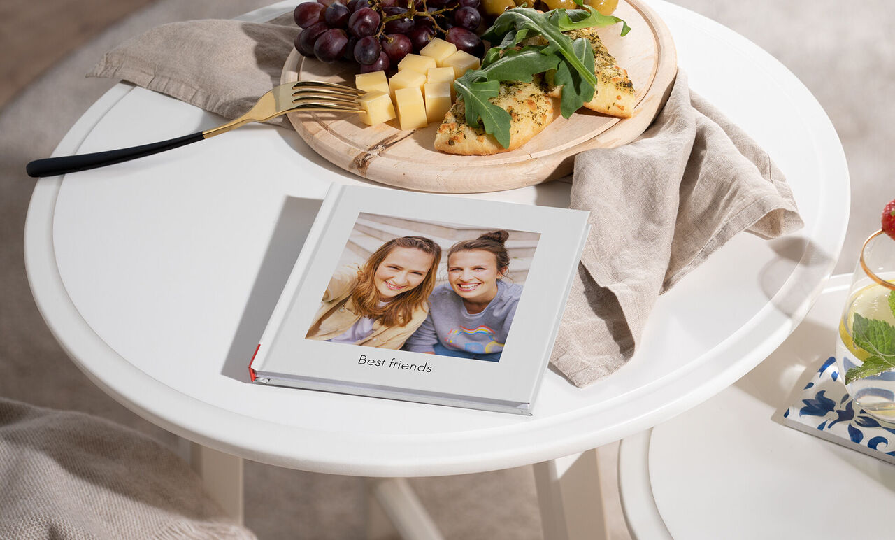 Starostlivo navrhnutá fotokniha s názvom „Best friends“ na stole, obklopená ovocím a dobrotami.