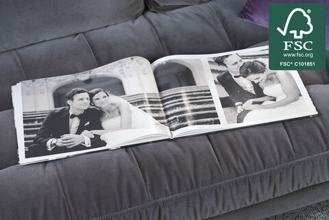 Otvorená CEWE FOTOKNIHA ukazuje romantické svadobné fotografie na pohovke v elegantnom prostredí.