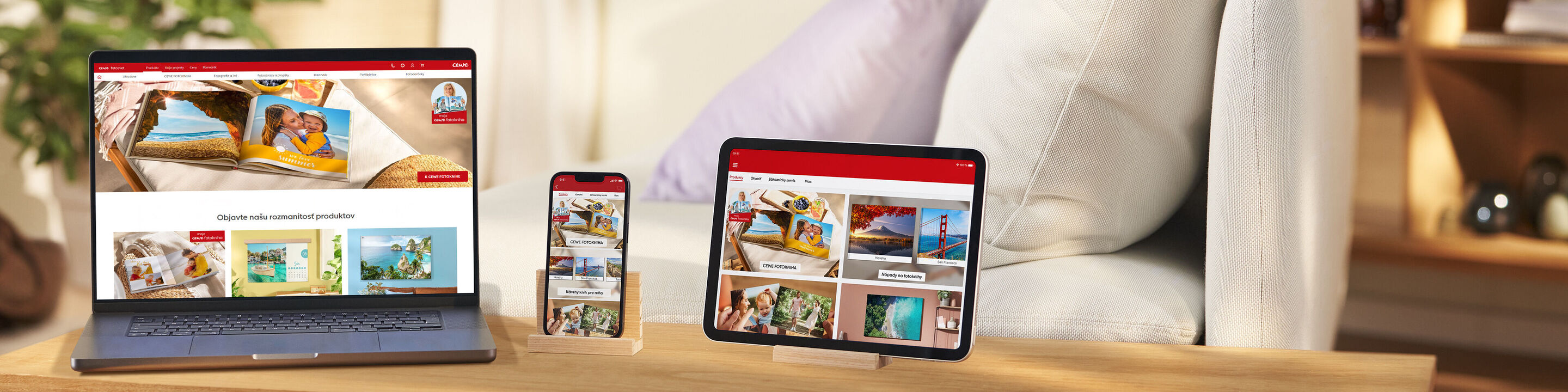 Laptop, tablet a telefón ukazujú CEWE fotoworld na drevenom stole.