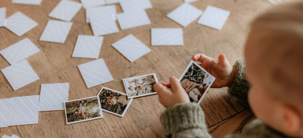 Dieťa si prezerá fotografie, obklopené prázdnymi kartičkami na stole