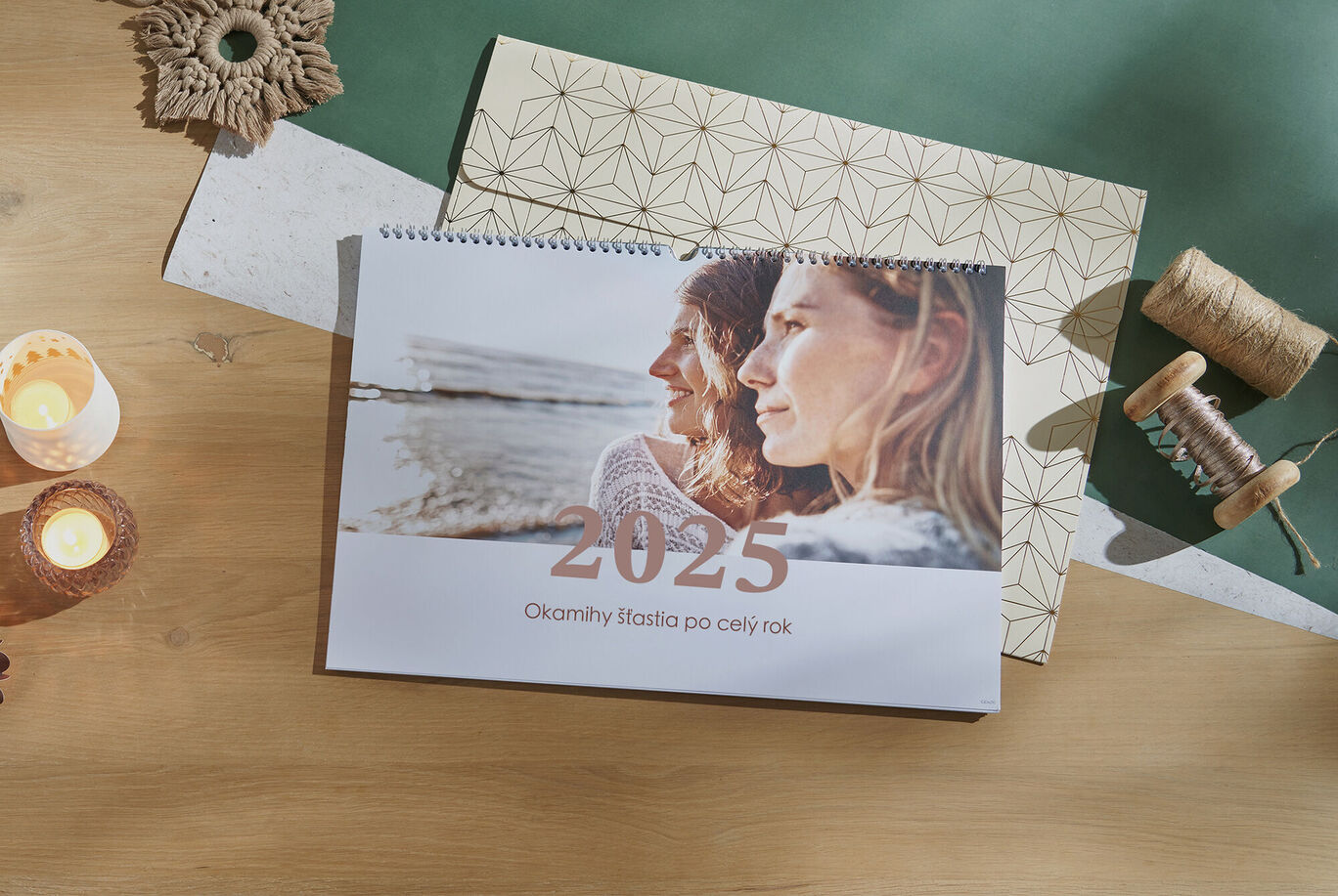 Elegantný kalendár na rok 2025 na stole, obklopený dekoráciami a sviečkami.