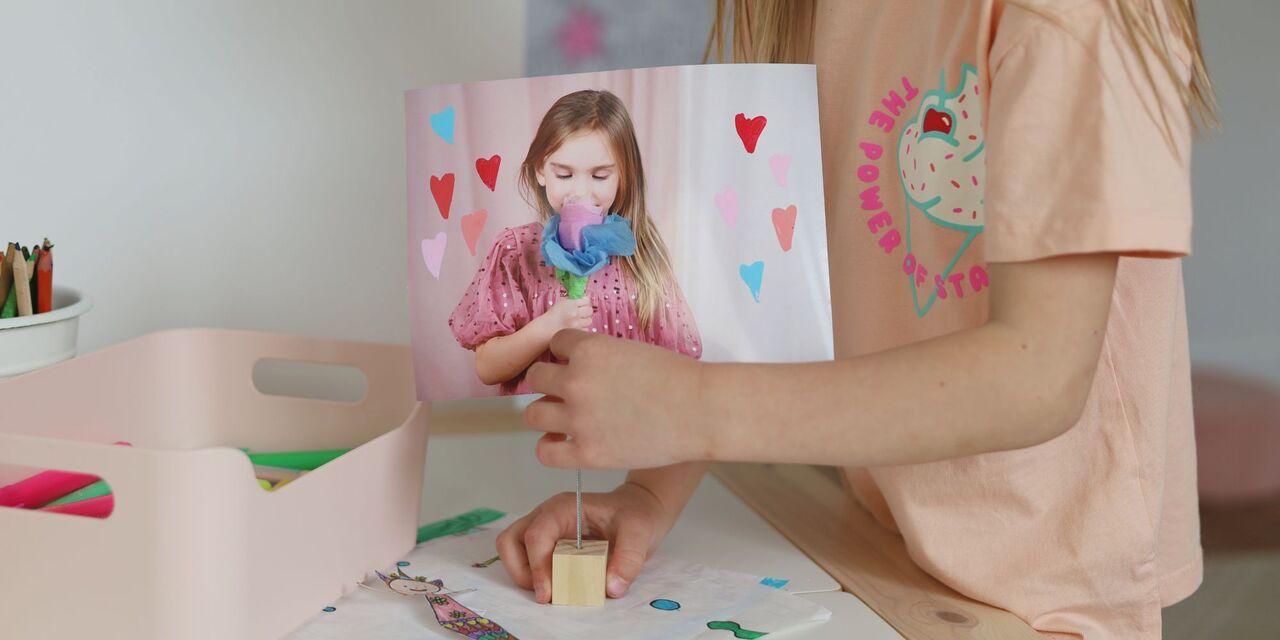 Dieťa drží fotografiu so srdiečkovými motívmi a usmieva sa. Kreatívne a radostné spracovanie.