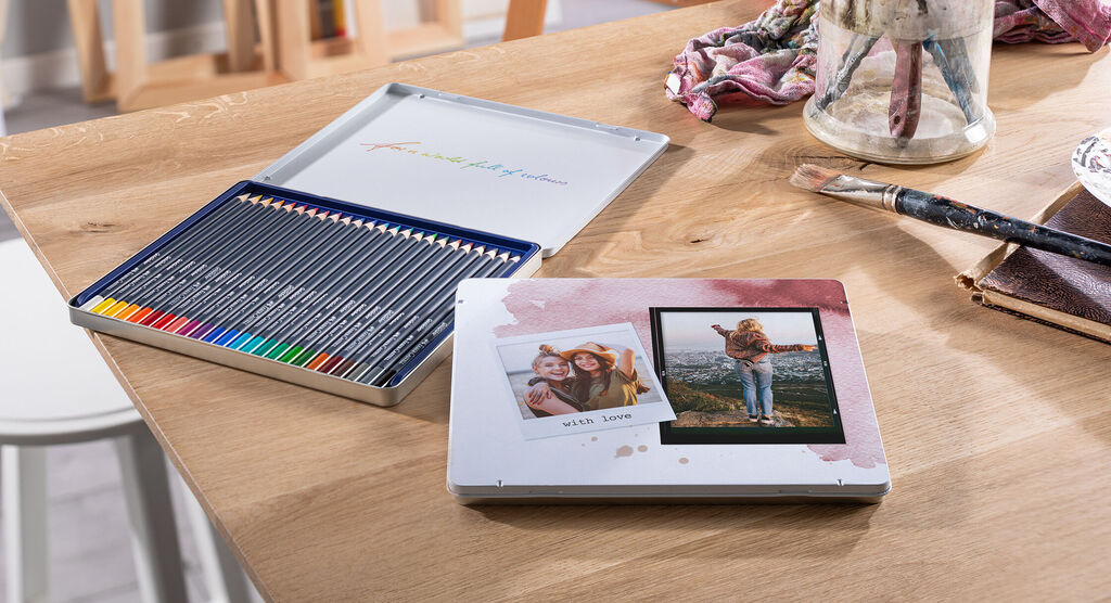 Farebné pastelky v kovovej dóze vedľa fotoknihy s pamätnou fotografiou