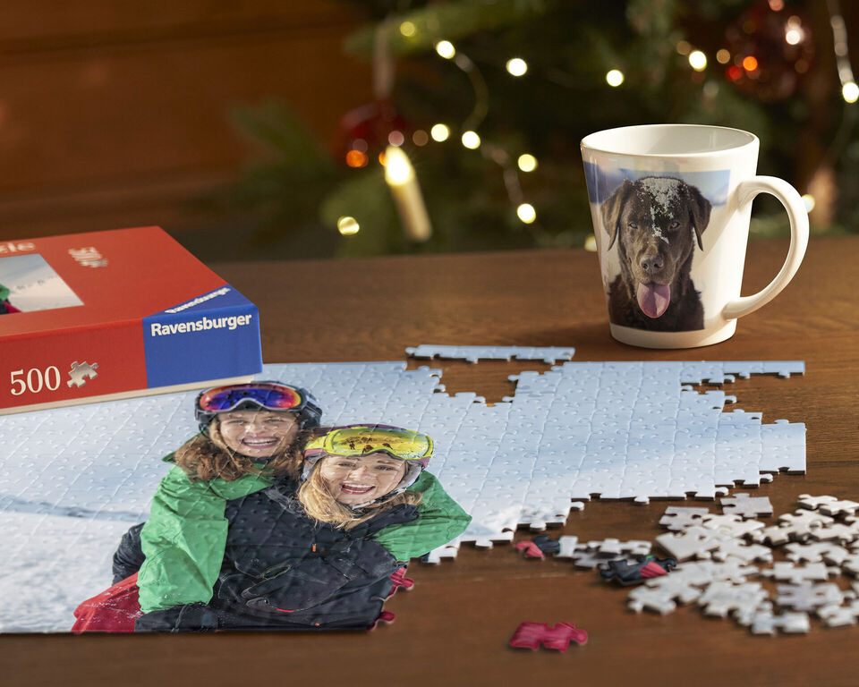 Puzzle na stole s dvoma ľuďmi v farebných bundách. Vedľa je šálka.