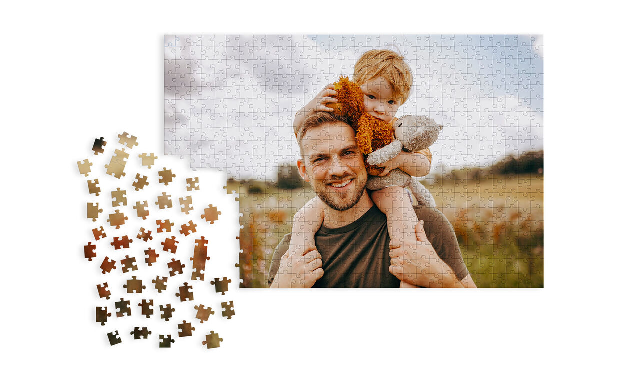 Puzzle zobrazuje otca s dieťaťom na rukách, obklopených malebnou krajinou.