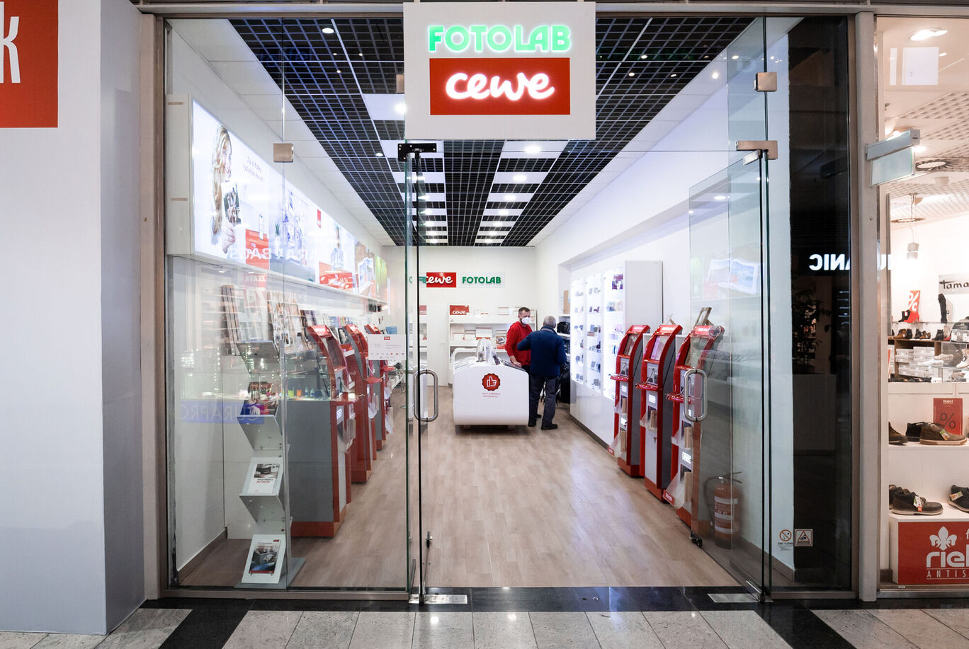 Vstup do CEWE fotolaboratória v modernom obchodnom priestore s návštevníkmi.