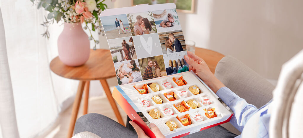 Osoba drží CEWE Fotobox s fotografiami a pralinkami v ruke.