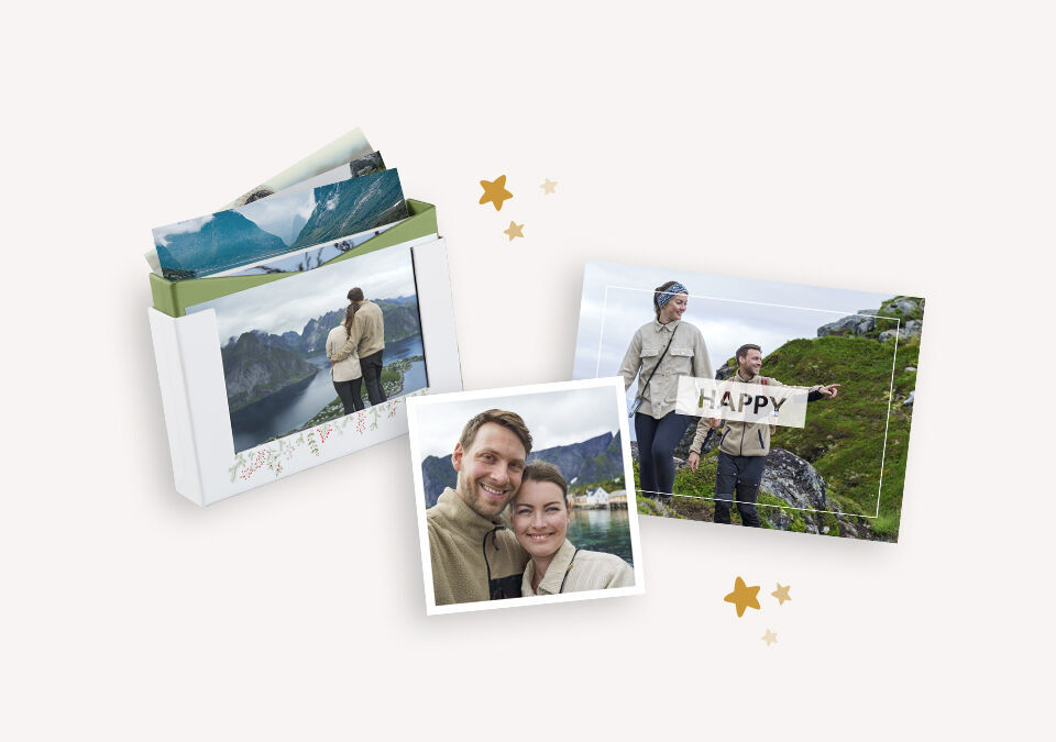 Pár drží tabuľku s nápisom 'HAPPY' v malebnej krajine. Vedľa je milá fotokniha.