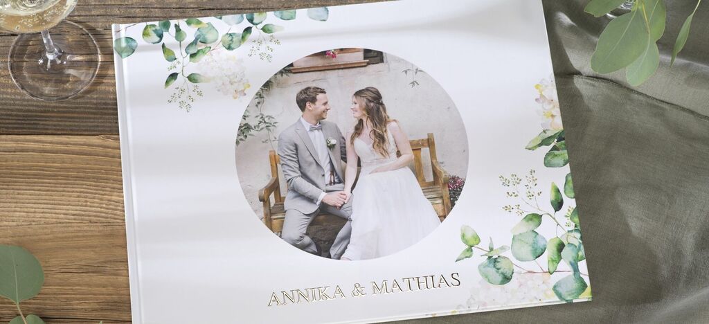 Svadobná fotokniha s párom v šatách a obleku, ktoré obklopujú rastlinné ornamenty.