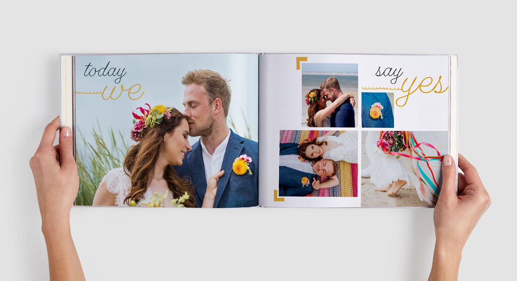 Pár drží fotoknihu so svadobnými fotografiami obklopenú farebnými kvetmi.