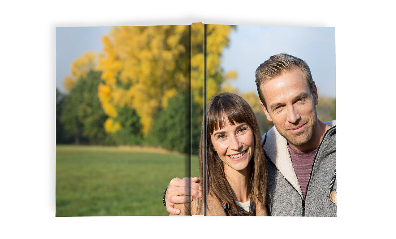 Pár drží fotoknihu v zelenom parku, obklopený jesennými stromami.