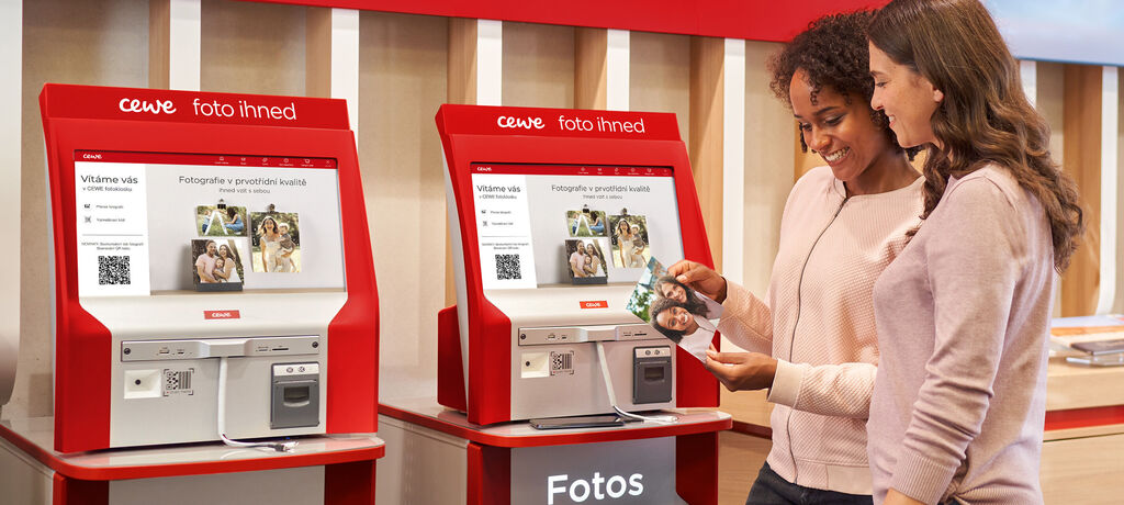 Dvaja ľudia používajú fotoautomat CEWE na úpravu a výber fotiek