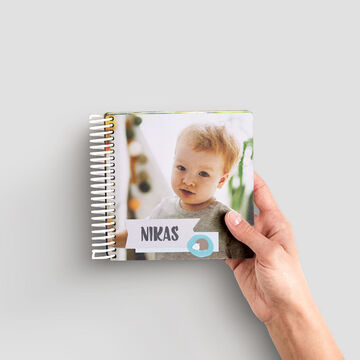 Ruka drží CEWE fotoknihu s menom Nika na obale.