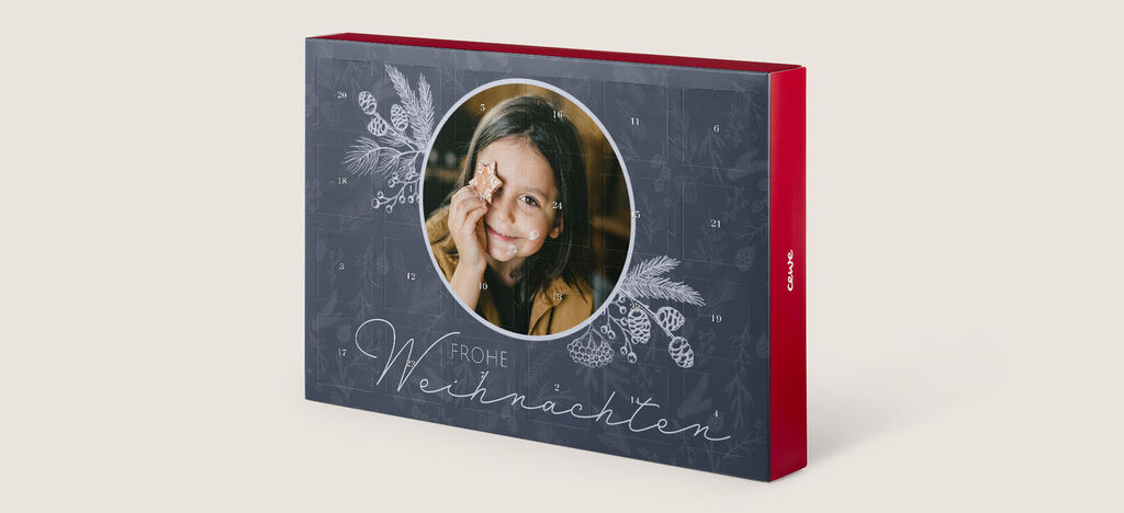 Otvorená CEWE fotokniha s vianočným dizajnom, ozdobená jedľovými vetvami a elegantným písmom.