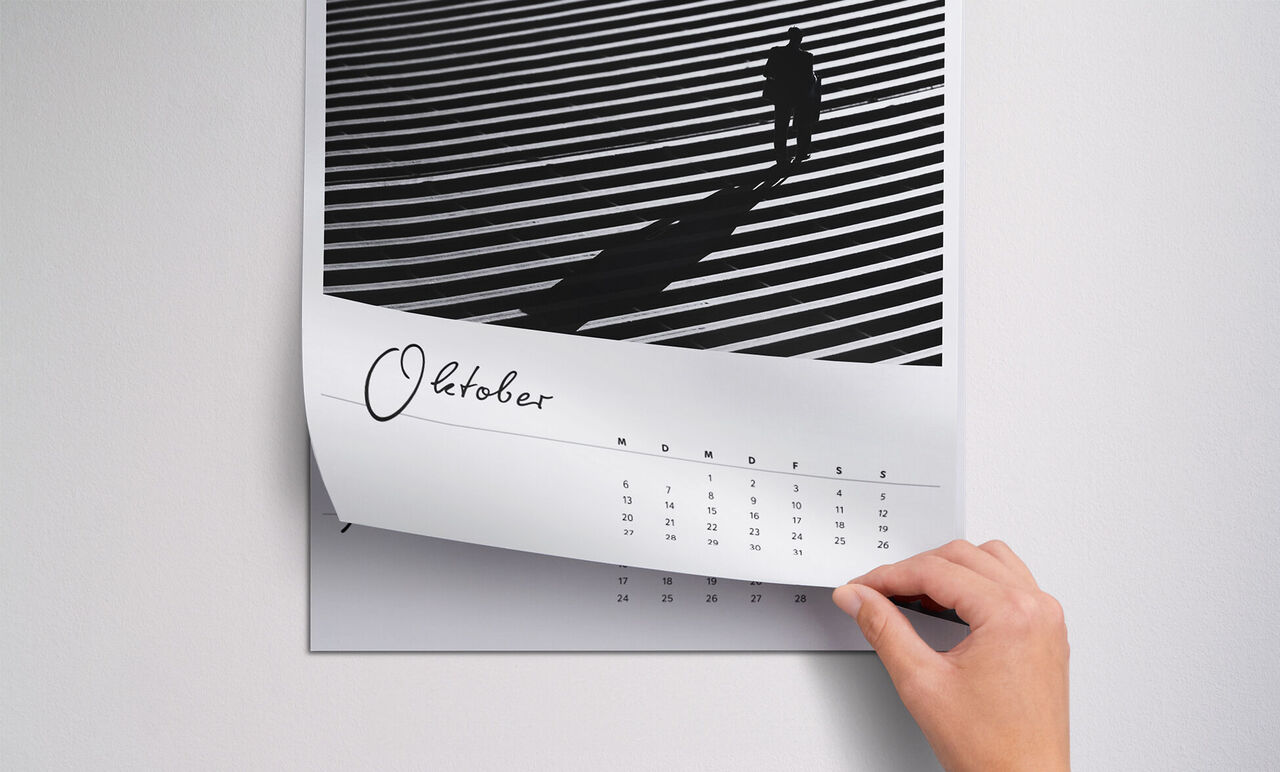 Ruka listuje stránkou fotokalendára s čiernobielymi čiarami a osobou v tieni. Viditeľný je október.