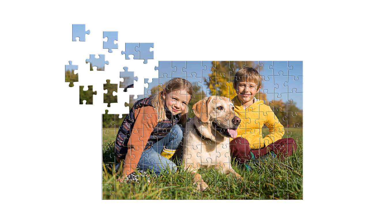 Dve deti na záhrade so psom, obklopené kúskami puzzle